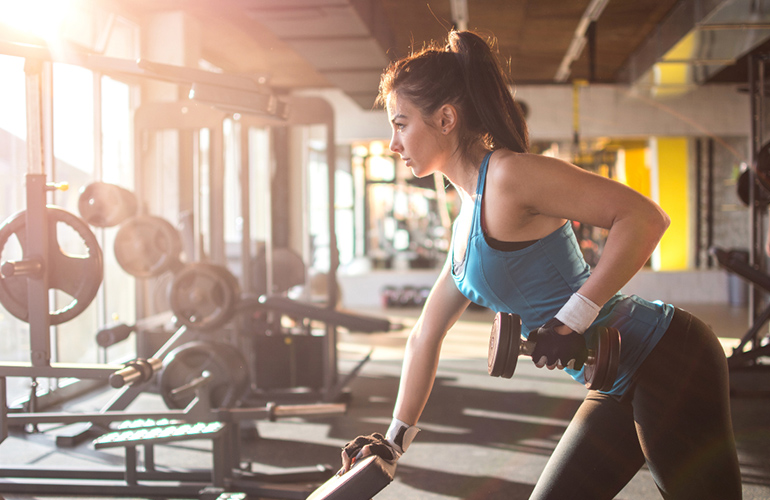 Sporty girl lifting weights in gym.